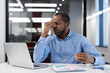 © Liubomir - Stressed african american male businessman holds glasses, experiencing work frustration at laptop in office setting. Reflects stress and fatigue from professional challenges.