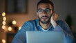 © NaphakStudio - thoughtful man with glasses gazes at his laptop in dimly lit room, reflecting on his work or ideas. warm glow of lights adds cozy atmosphere.