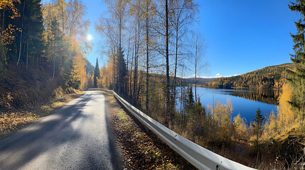 Poster - A panoramic view of an autumn forest road with a white guardrail, next to a lake and trees, under a blue sky with sunshine and white clouds