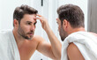 © Volodymyr - Man applying cosmetic face cream on mirror. Facial treatment. Portrait of man with bare naked shoulders touching skin. Sexy man with skin care product. Male face creme. Perfect skin, morning routine.