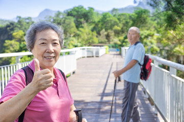 Wall Mural - Happy asian senior couple hiking in the nature and showing thumbs up