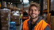 © jodoto - Cheerful Warehouse Worker in Orange Safety Vest Standing Amidst Stacked Boxes and Pallets in Industrial Setting