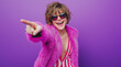 © Graphique - Photo of a young woman wearing a white T-shirt, a pink fluffy coat, and striped wide-leg pants, standing on a purple background with an open mouth and pointing her finger to the side.