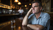 © Crystal - Man sitting alone at dimly lit bar, holding glass of whiskey with thoughtful expression, empty bar stools and distant bartender visible. Reflective solitude and introspection in a quiet bar setting