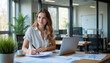 © Gavasol - Businesswoman working diligently at her desk with a laptop and documents in a modern office