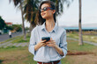 © SHOTPRIME STUDIO - Woman in sunglasses standing on road near palm tree, holding cell phone, and looking intently at screen