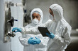 © Seventyfour - Side view of female process technician in hazmat suit using tablet computer inspecting stainless tanks with colleague while controlling fermentation process at craft cider factory, copy space
