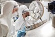 © Seventyfour - Medium shot of African American female process technician in mask opening tank lid while inspecting product fermentation with colleague in factory workshop, copy space