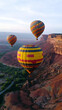 © Mohan - Three colorful hot air balloons float over a rugged landscape.