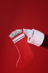 Wall Mural - Santa holding stocking with dollar banknotes on red background, closeup