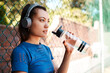 © peopleimages.com - Sports, woman and drinking water with headphones for music, fitness playlist or motivation with podcast. Fence, athlete and thinking with h2o for thirst, hydration or listen audio in basketball court
