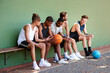 © peopleimages.com - Bench, basketball and people on court for break, fitness exercise and wellness in sports match. Relax, athletes or group of healthy players resting with ball for performance, workout or outdoor game