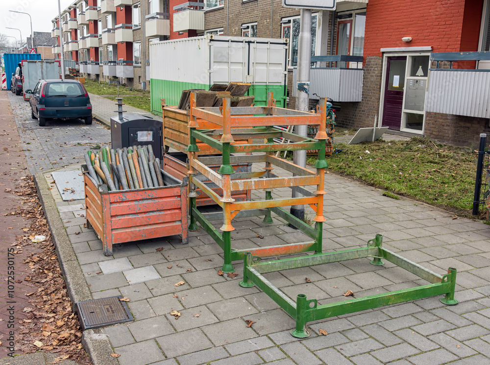 Scaffolding parts lie outside in steel racks on the sidewalk in a residential area