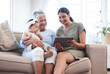 © peopleimages.com - Granny, mother and baby on sofa, tablet and relax with happiness, bonding together and smile. Family, generations and mama with kid, technology and house with infant, online video and digital app
