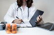 © Orathai - Female doctor holding a medicine bottle is checking the quality of medicine for any side effects the patient or not and recording patient information at the hospital. medical and health care concept