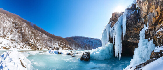 Poster - stunning frozen waterfall cascades down mountainside, surrounded by snow covered trees and clear blue sky, creating serene winter landscape