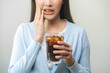 © KMPZZZ - Health asian young woman touching her mouth, expression, suffering from toothache, decay or sensitivity cavity molar tooth or inflammation drink cold, sparkling water at home. Sensitive teeth people