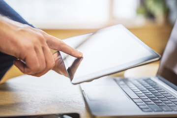 Poster - Male finger gently tapping the screen of a sleek digital tablet lying on a desk, within the unfocused brightness of a contemporary office