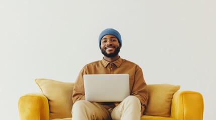 Wall Mural - A man wearing a blue hat is sitting on a couch with a laptop in front of him