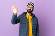 © luismolinero - Skier man with snowboarding glasses over isolated purple background saluting with hand with happy expression