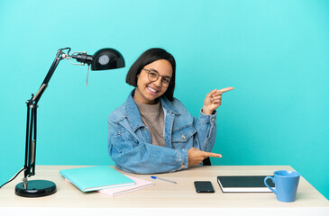 Wall Mural - Young student mixed race woman studying on a table pointing finger to the side and presenting a product