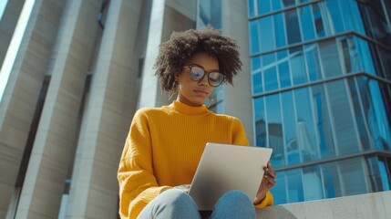 Poster - A woman in a yellow sweater is sitting on a ledge with a laptop in front of her