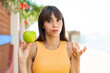 © luismolinero - Young woman with an apple at outdoors making doubts gesture while lifting the shoulders