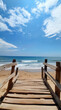 © PhotoArtHub - A wooden walkway leads to the beach on a sunny day. The blue sky is dotted with white clouds and the ocean waves are crashing gently on the shore