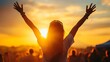 © Copi - A woman with her arms raised stands in front of a crowd of people at a concert, with the sunset behind the stage.