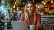 © somchai20162516 - A young woman sits working at a cafe table with a laptop, one hand holding a cup of coffee, her face showing her determination in her work amidst a lively and relaxing atmosphere.