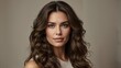 © Lira - Portrait of a woman with voluminous, wavy brunette hair and a subtle makeup look placed against a neutral background