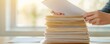 © Naphol - A person organizing a stack of papers, showcasing productivity and office work environment in a bright setting.