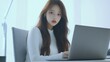 © tope007 - A beautiful young Korean woman is sitting at her desk in an office, wearing a white long-sleeved shirt, working on a laptop computer, AI Generative