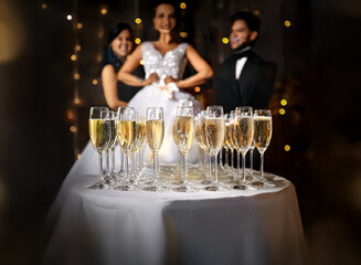 Poster - A table with champagne flutes filled with sparkling wine,  in the foreground, with a bride and two guests in the blurry background.