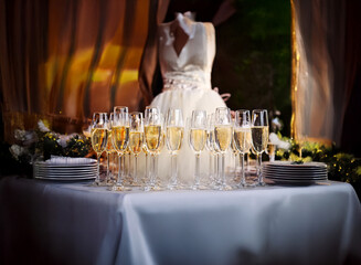 Poster - A table set for a celebration with champagne flutes and plates, a white dress is seen in the background.