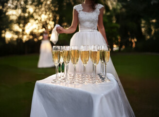 Poster - A bride in a white wedding dress stands next to a table full of champagne flutes, ready to celebrate with her guests.