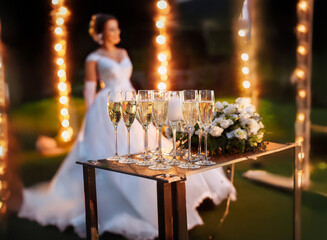 Poster - A bride stands in the background of a wedding reception, a tray of champagne flutes and white flowers in the foreground.