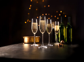 Poster - Four champagne flutes filled with bubbly sit on a dark surface with two bottles of wine and festive lights in the background.