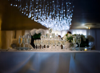 Poster - A champagne tower stands on a white tablecloth in a dimly lit room. White flowers and sparkling lights add ambiance to the celebration.