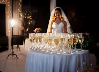 Poster - A bride in a white wedding gown smiles as she stands behind a table with champagne flutes.