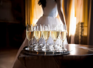 Poster - A tray of champagne glasses sits on a table in front of a bride in a white wedding dress.