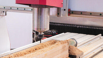 Fototapete - A woodworking machine is cutting a piece of wood. The machine is red and silver. The wood is being cut into a shape
