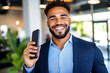 © Tanya - Confident smiling African American businessman in blue suit using his mobile phone in a stylish office, demonstrating professional work habits and connectivity. Copy space.