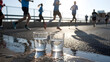 © @ArtUmbre - Runners passing by water cups during an outdoor marathon under bright sunlight in a bustling urban environment
