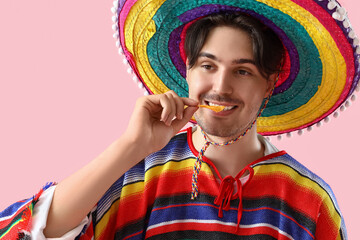 Wall Mural - Young Mexican man eating nachos on pink background