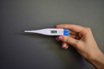 Female hand with electronic thermometer on dark background