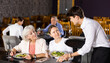 © JackF - Amiable young waiter serving ordered dishes to carefree female friends gathered over dinner in restaurant