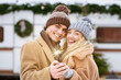 © Prostock-studio - A young couple smiles joyfully while holding a sparkling sparkler. They are dressed warmly for winter and surrounded by festive decorations outdoors.