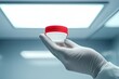 © zakiroff - A hand in a medical glove holds a red-lidded specimen container in a clinical setting under bright overhead lights