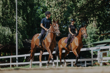 Two young equestrians ride their horses through a lush green park on a sunny day. The scene captures the joy and connection between humans and animals in a natural setting.